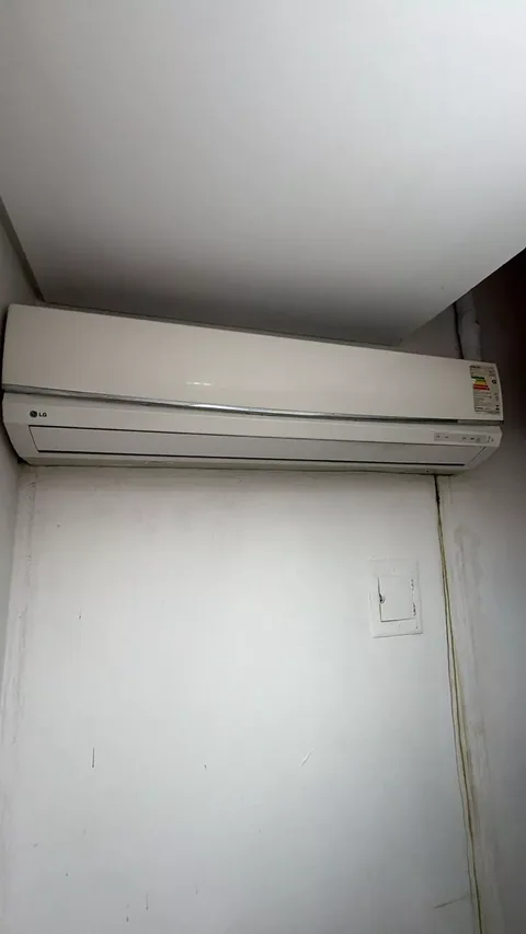 Unidade interna split LG branca montada em parede clara, próxima ao teto, com selo de eficiência energética e tubulação isolada saindo atrás do aparelho