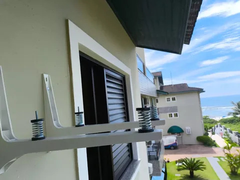 Suportes metálicos brancos para condensadora em parede externa com molas amortecedoras de vibração; vista de telhados e mar ao fundo