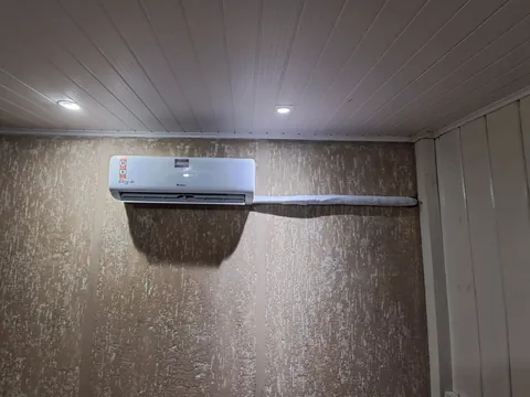 Evaporadora split Gree em parede texturizada bege sob forro de PVC branco com spots de LED; tubulação isolada à direita